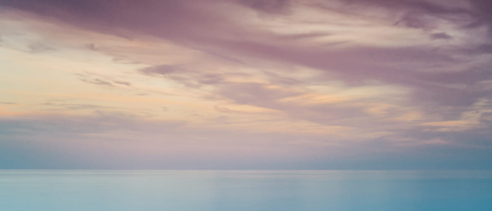 Serene seascape with pastel tones in the sky, blending hues of purple, pink and blue.