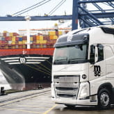 An MSC-branded truck parked at a port with an MSC cargo ship loaded with containers in the background.