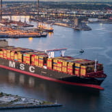 An MSC cargo ship loaded with shipping containers navigating through a port.
