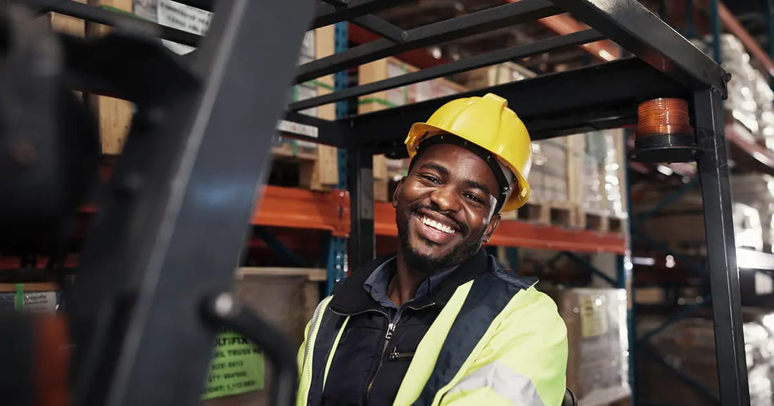 An AGL employee wearing a yellow hard hat and reflective jacket in a warehouse.