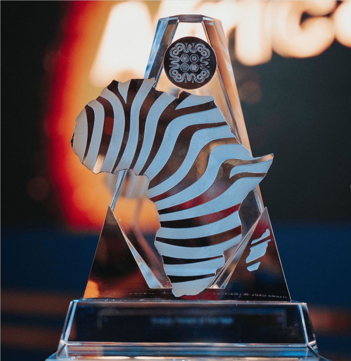 A glass award faces the camera, displaying a silhouette of the African continent. 